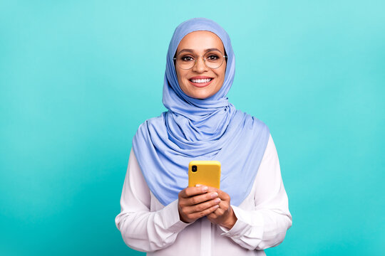 Photo of pretty charming young woman wear arab headscarf spectacles chatting modern gadget isolated turquoise color background