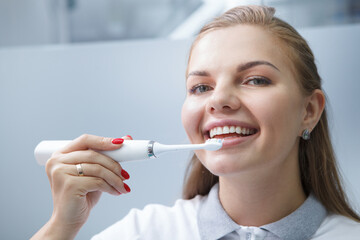 Close up of a charming young female dentist smiling, using electric toothbrush on her teeth