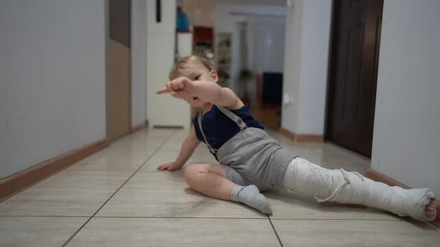 Happy cute toddler, after an accidental fracture of his leg, moves around the apartment with a plaster cast. Recovering a broken leg at home, medical insurance concept