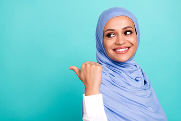 Photo of adorable dreamy young lady dressed islamic hijab smiling looking pointing back empty space isolated teal color background