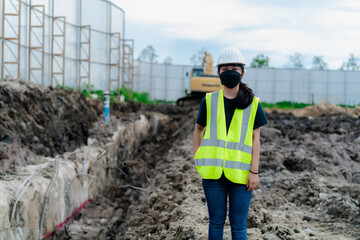 Portrait of an Asian female engineer wearing a bright green shirt and standing in a white helmet at the construction site