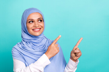 Photo of charming pretty young lady dressed islamic hijab smiling pointing lookig empty space isolated teal color background