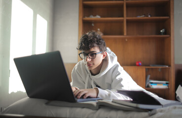 young boy studies in his bedroom on books and laptop