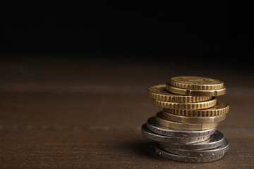 Many Euro coins stacked on wooden table against black background, space for text