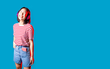 serene asiatic woman isolated on blue  background listening music with bluetooth headphones smiling...