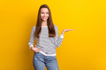 Obraz premium Photo of optimistic brunette millennial lady hold empty space wear white sweater isolated on yellow color background