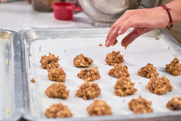 Woman places uncooked raw oatmeal cookies on steel tray.