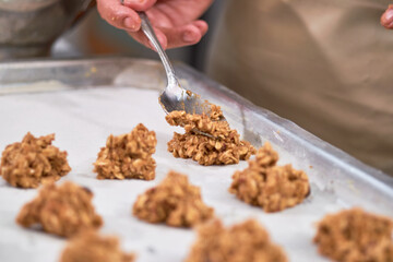 Woman places unbaked oatmeal cookies on steel tray.