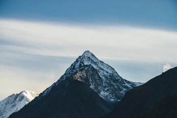 Obraz premium Sunny landscape with great mountains silhouettes and snow-covered pointy peak with golden sunshine on rocks. Mountain with peaked top with snow in sunshine. Beautiful pointed pinnacle in sunlight.