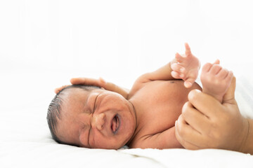 Newborn baby crying on white bed while mother’s hands takes care carefully. Family, love and new life concept