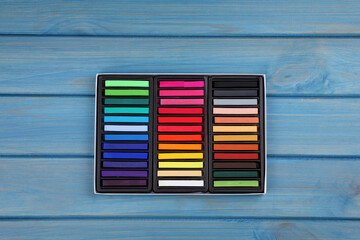 Set of colorful pastels in box on light blue wooden table, top view. Drawing materials