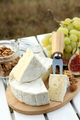 Delicious cheese, nuts and fruits on white wooden table outdoors