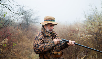 hunter man with a gray beard in hunter suit load cartridges in a double-barreled rifle