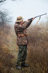Fototapeta premium hunter man with a gray beard in hunter suit makes aiming wiring with a double-barreled rifle 