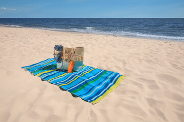 Fototapeta na wymiar Striped beach towel and bag with accessories on sandy seashore, space for text