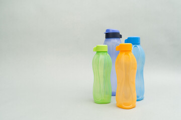 Plastic Tupperware Bottles. A stack of colour water bottles, blue, orange and green, gathered on the right side, on a grey background.