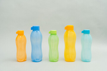 Plastic Tupperware Bottles. A stack of colour water bottles, blue, orange and green on a grey background arranged in a straight line.