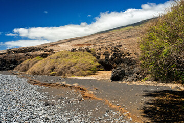 Lava rocks pile up along the high tide line of a small beach to meet the ocean and sky on the southern shores of Maui Hawaii