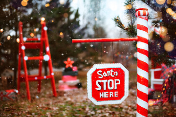 Outdoor road barrier in Christmas decorations in pine trees with the inscription Santa, please stop...