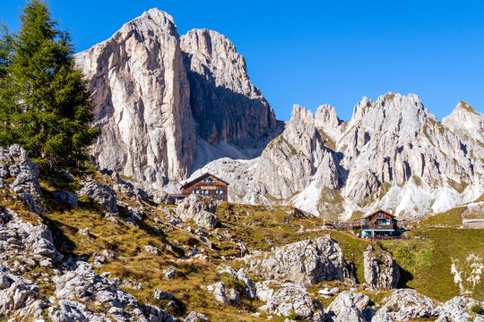 Panoramic view of Catinaccio - Rosengarten mountain group in autumn with two mountain huts visible at the base of the high dolomite peaks. Roda di Vael, South Tyrol - Italy