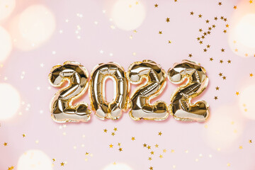 New year 2022 balloon celebration card. Gold foil balloon number 2022, party decoration, gold confetti on pink background. Flat lay, merry christmas, happy holidays concept.