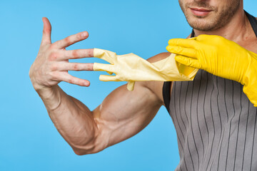 man in apron with pumped up body rubber gloves cleaning blue background