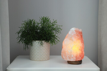 Beautiful Himalayan salt lamp and green houseplant on white table in room