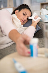 woman with flu layed on sofa reaching for medication