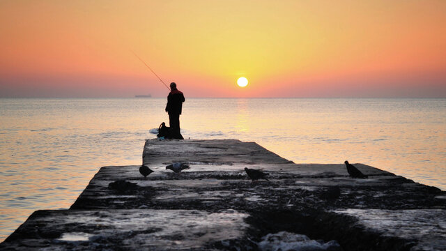 Рыбак ловит рыбу в море на рассвете