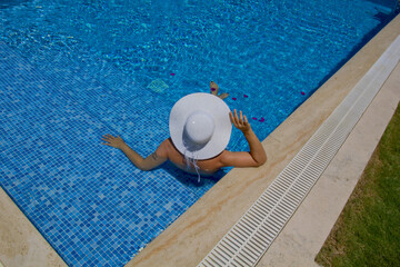 Fototapeta na wymiar young woman in a hat relaxing in a swimming pool