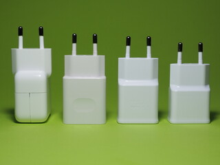 Comparison of smartphone charger adapters. Different size and power chargers on a green background.