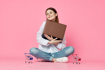 cheerful woman with laptop sitting on the floor on a pink background