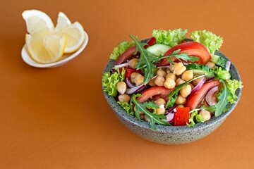 Healthy Vegetarian Chickpea Salad
in a bowl with vegetables, herbs and dressing on an orange (terracotta) background. Healthy food concept.