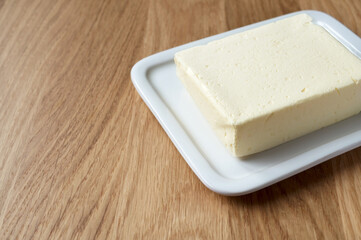Butter on white butter dish on wooden background, copy space. Made from cow milk.
