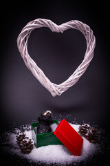 A dog in a red-green box in the snow with pine cone, looking at the white heart above, on a dark background. Text space. Christmas, New Year, Dog paw, concept. Minimal style.