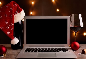 Laptop computer on table surrounding by Christmas decorations, a glass of red wine and wine bottle...
