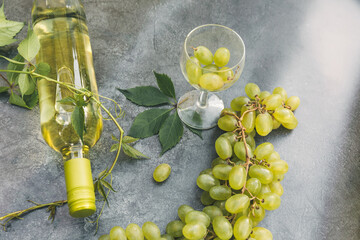 Top view of bottle white wine, green vine, wineglass and ripe grape on vintage gray stone table...