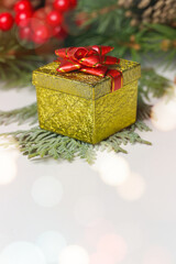 Small golden gift box with red bow and Christmas decoration, close up.