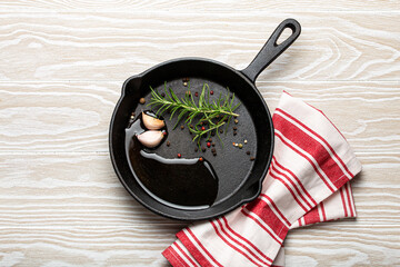 Black cast iron frying pan with ingredients for cooking: oil, fresh green rosemary, raw garlic...