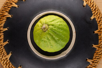 One organic juicy bergamot on a ceramic dish, close-up, top view.