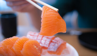 Using chopsticks, salmon sashimi. Sashimi is a popular dish of Japanese restaurants.