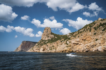 Fototapeta na wymiar Tourist day trip pleasure boat moves along beautiful cliff landscape with white clouds in sky. Balaklava. Black sea Crimea