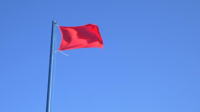 Red flag symbolizing ban on bathing waving with blue sky background. Video 4K