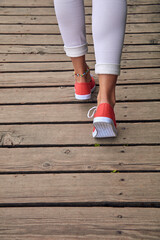 Fototapeta na wymiar Woman in red shoes and white jeans on wooden boards.