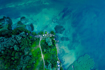 Bird's eye view of the lake and green forest. Aerial landscape of the shallow blue water and camping site.
