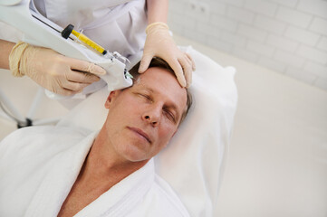 Therapist doing facial mesotherapy treatment on middle aged handsome Caucasian man in a modern...