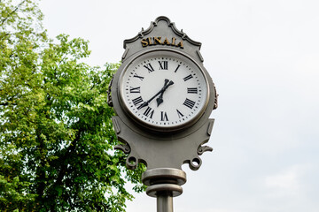Fototapeta na wymiar Vintage style grey metallic clock towards cloudy sky in Sinaia Park, Romania, in a rainy summer day.