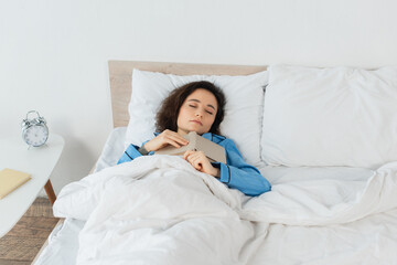 brunette woman in blue pajamas sleeping with book in bed.