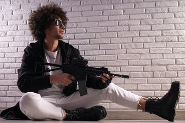 an Arab with an African hairstyle in stylish fashionable clothes with an airsoft gun poses against...