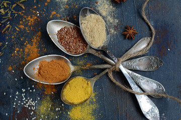 Vintage metal spoons with various types of spices on an old textured background. Selective focus. View from above